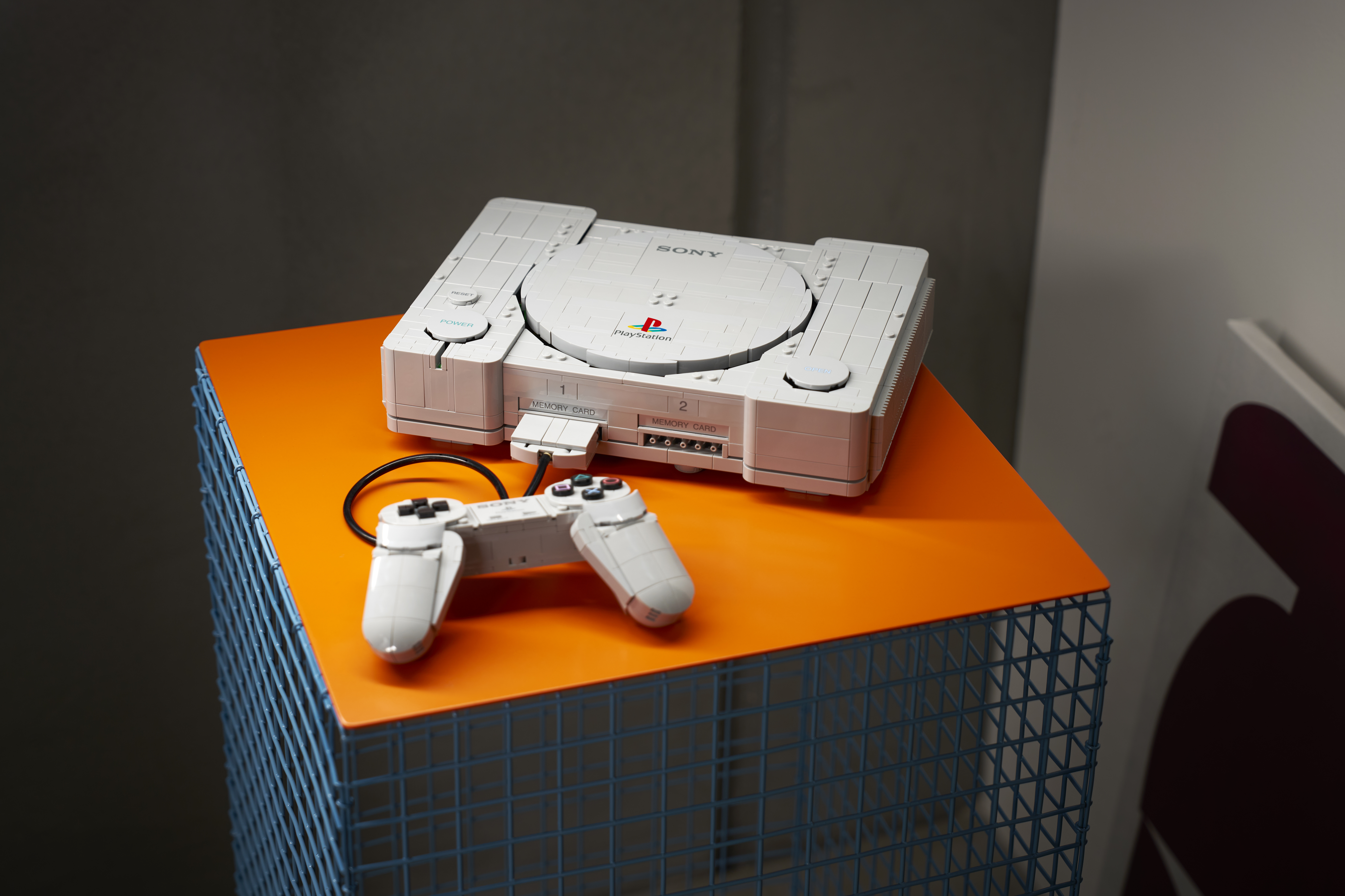 Modelo de PlayStation y mando construidos con piezas LEGO sobre una mesa naranja.