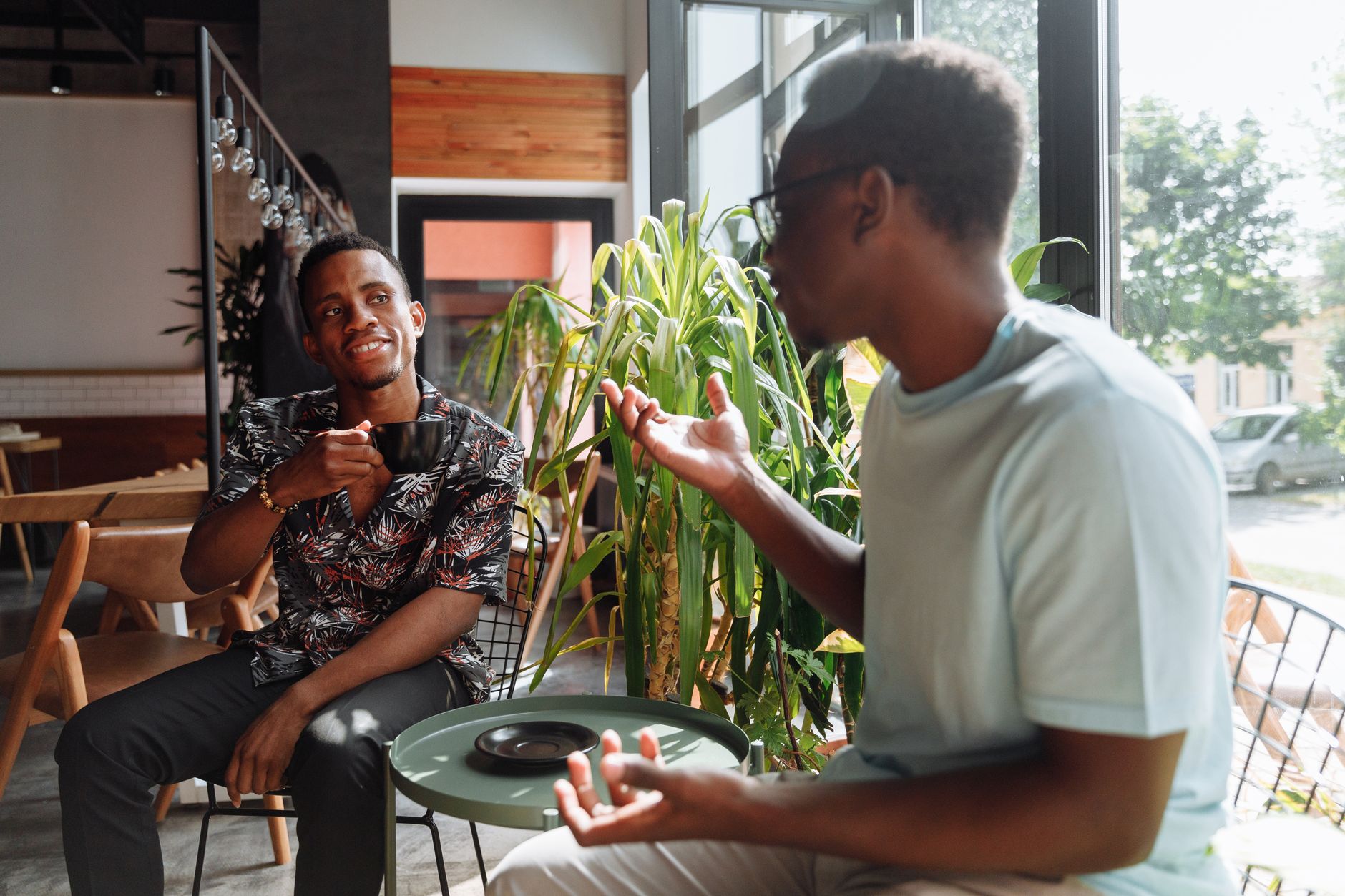 Dos personas conversan con una taza de café junto a una ventana.